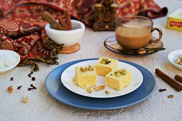Indian sweets with pistachios, almonds and cardamom on a white plate on a light concrete...