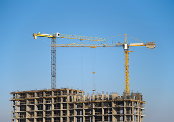 Hydraulic luffing jib tower cranes and workers being poured concrete into foundation. Cement pouring into formwork of building at construction site. Tower cranes constructing a new residential build