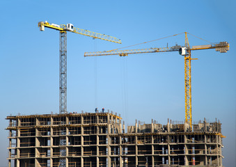 Hydraulic luffing jib tower cranes and workers being poured concrete into foundation. Cement pouring into formwork of building at construction site. Tower cranes constructing a new residential build