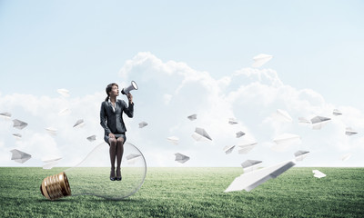 Woman with megaphone sitting on big light bulb
