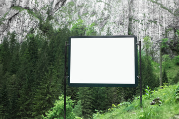 Advertising billboard with empty white mockup in green forest of mountains.