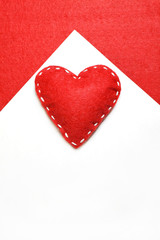 Red felt heart with white stitches. A symbol of love handmade sewn with thread around the edge on a white background.