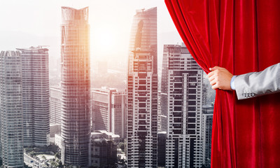 Modern business cityscape behind curtain opened by businessman hand