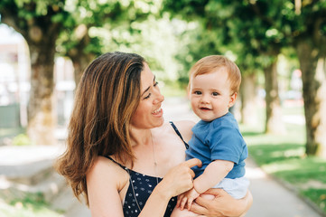 Outdoor portrait of happy mother holding adorable baby boy in arms