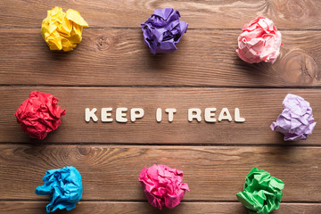 Keep it real phrase on wooden table and paperballs around
