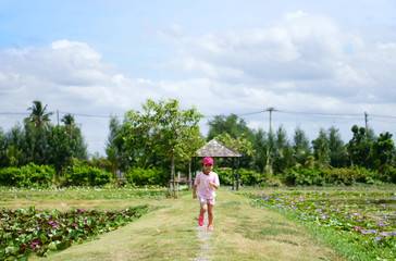 Asian child cute or kid girl fun running and jogging on nature meadow or green grass and lotus field for sport exercise and play healthy with energy on sunny hot weather and wear pink cap and shirt