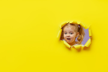 Little surprised child looking, peeping through the bright yellow paper hole. Advertise childrens...