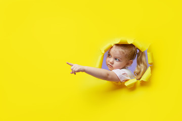 Little surprised child looking, peeping through the bright yellow paper hole. Showing hand to side....