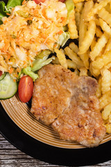 Fried pork chop in breadcrumbs, served with fries and salad.