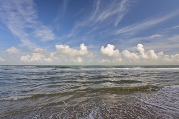 Fale na brzegu morza, niebieskie niebo i białe chmury w słoneczny letni dzień. - obrazy, fototapety, plakaty