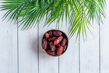 Royal dates fruit in a bowl of coconut in palm branches and leaves on a white wooden table.