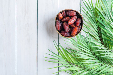Royal dates fruit in a bowl of coconut in palm branches and leaves on a white wooden table.