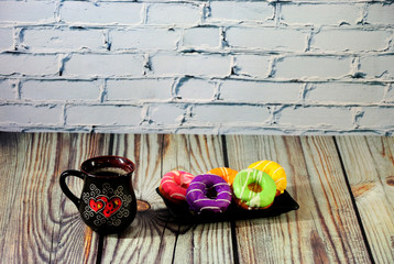A black ceramic cup with fresh cappuccino and a plate with five donuts in colored glaze on a wooden...