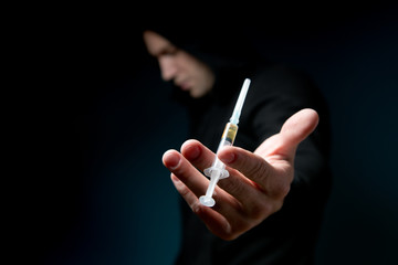 dark silhouette of a man holds out a frame with a dose of drug in a syringe