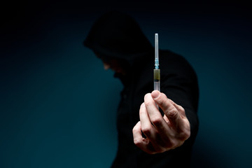 A man holds out a syringe with a drug and hides his face