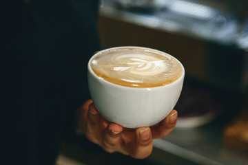 Close-up of a barista holding a cup of freshly brewed coffee in his hand.