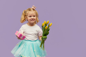 Smiling child girl with spring flower bouquet and greating card on purple background. Little...