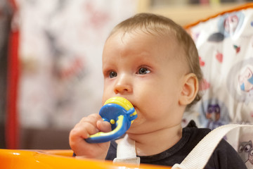a small child eats and sits and holds the edge of the feeding table in the nursery, grimy and stained with food, baby food concept, complementary foods, the first spoon, nibbler, fruit feeder pacifier