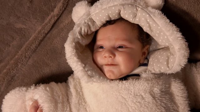 Adorable little baby in a white plush teddy bear custume lay on the blanket