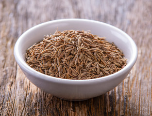 Cumin seeds in white bowl on wooden table