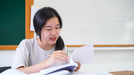 Happy teenage Asian students laughing feeling excited, so glad when doing project homework or work approved successful,sitting at front green board looking happiness in positive good with textbook