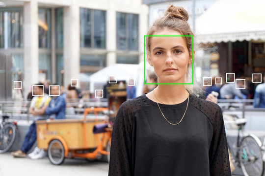 young woman picked out by face detection or facial recognition software - several other faces detected in crowd of people in background