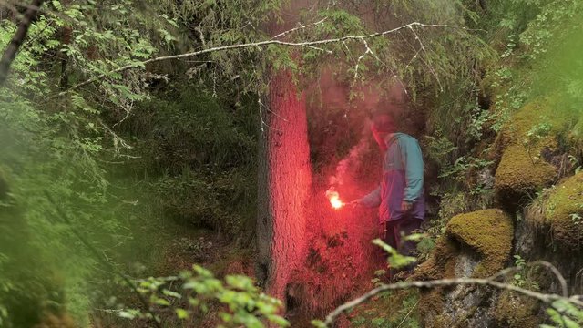 Lonely young hiker man got lost in the forest and trying to survive with the help of red burning signal flare. Stock footage. Wild nature and SOS situation concept.