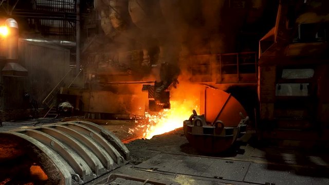 Molten iron flowing in a steel mill with many sparcles flying into the sides. Stock footage. Hot shop of the steelmaking factory with professional machinery.