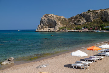 Fototapeta na wymiar Stegna beach on Greek island Rhodes with sand, sunshades and boats in the background