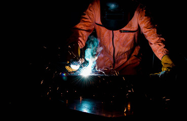 Fototapeta na wymiar A man wearing safety mask and suit is welding metal