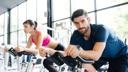 Fototapeta na wymiar Men and women wear sportswear, workout ride a bike in gym, with the intention of healthcare. Cycling to make body healthy With tight muscles And reduce the weight good. sports and healthcare concept