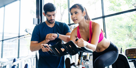 Fototapeta premium Asian Women wear sportswear, workout ride bicycles in gym, with the intention of health care. With a trainer to advise By cycling to make the body healthy With tight muscles And reduce the weight good