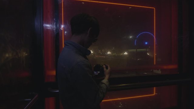 Asian male taking picture of the view from an elevator at night.