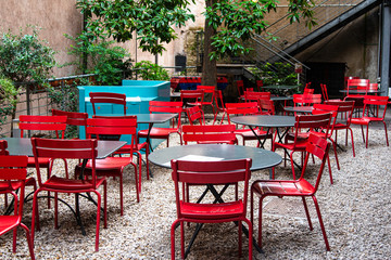 Fototapeta na wymiar Bright red metal chairs around grey tables on a stone patio with trees and stairs.