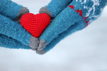 Valentine's day, red knitted heart in female hands in gloves on white snow background. Concept of romantic love, winter weather