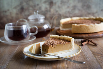 On a vintage plate, a piece of pumpkin pie and a spoon. In the background a delicious pumpkin pie with chocolate and a Cup of tea