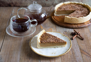 A piece of pumpkin pie on a beautiful plate, pumpkin tart on a wooden platter, and a Cup of hot tea on a wooden table.