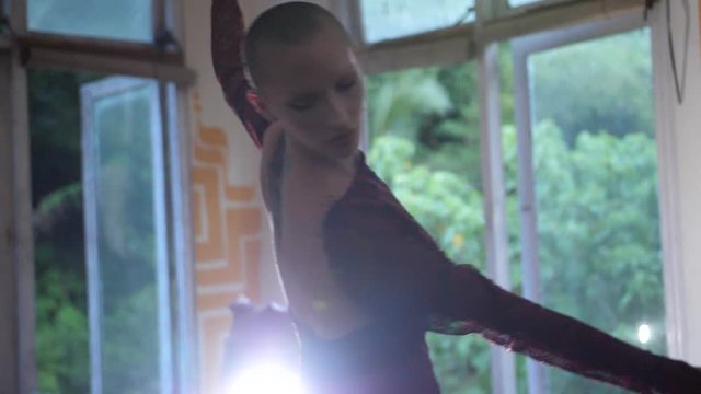 A mysterious young woman with shaved head is spinning around and dancing, looking sensual and intense towards the camera