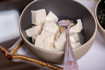 Square pieces of tofu cheese in a deep bowl with a spoon
