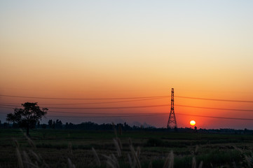 High voltage electric tower and transmission lines across the field when sunset. Electricity pylon.