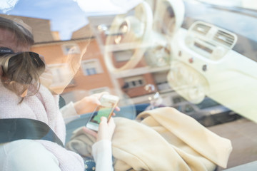 A young woman in the co pilot seat in a car texting with the mobile phone