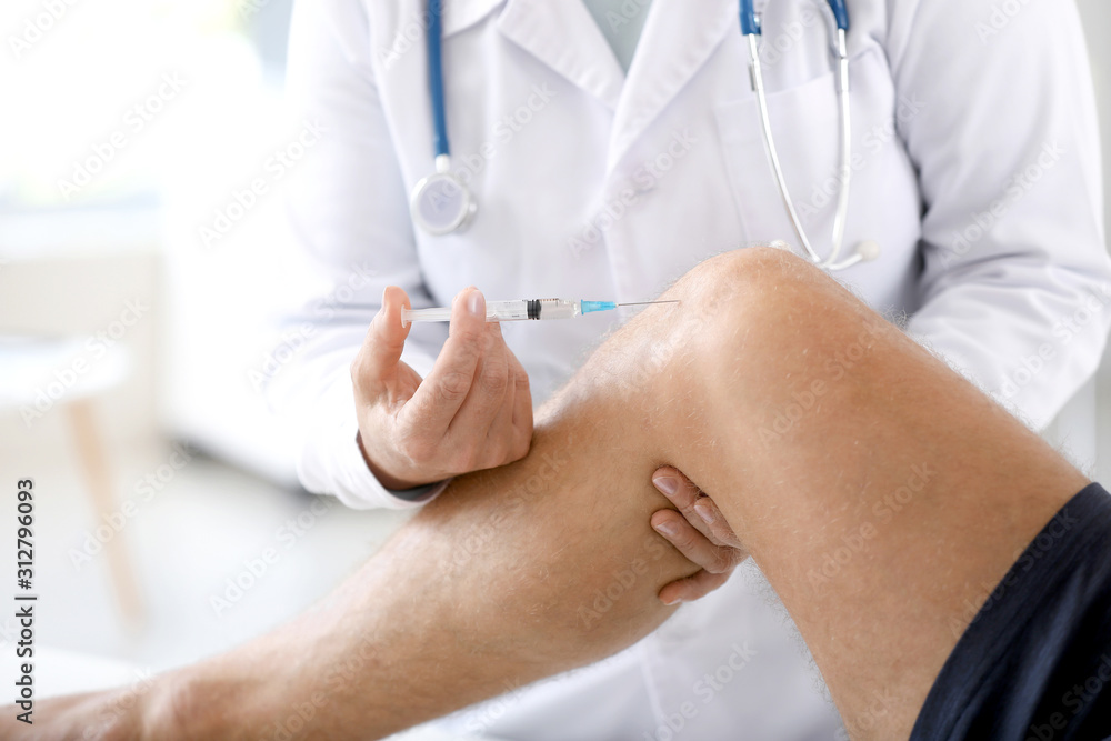 Wall mural doctor giving sportsman with joint pain injection in clinic, closeup