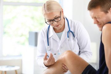 Mature doctor giving sportsman with joint pain injection in clinic