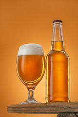 Bottle and glass of beer on table against color background
