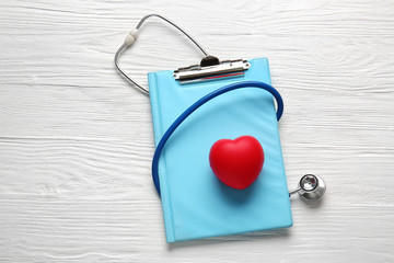 Stethoscope, clipboard and heart on wooden background