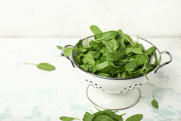 Colander with fresh spinach on table