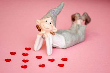 A happy, dreamy ceramic elf on a pink background with red hearts. Valentine's day. Love the concept.