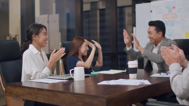 Millennial group of young businesspeople Asia businessmen and businesswomen celebrate giving five after dealing and signing contract or agreement at meeting room at small modern night office in city.