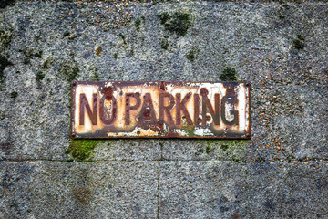 An old weathered No Parking sign on the side of a building