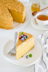 A slice of homemade honey cake with frozen berries on top on a white plate on a white table. Holiday cake. Traditional cake of Russian and Ukrainian cuisine. Vertical orientation.
